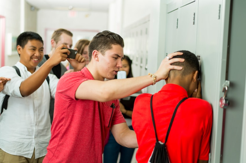 teenage boy slamming another teen boy into a locker while others watch and take photos