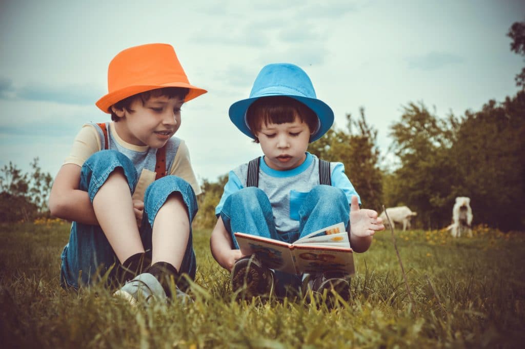 2 boys sitting on green grass looking at a book