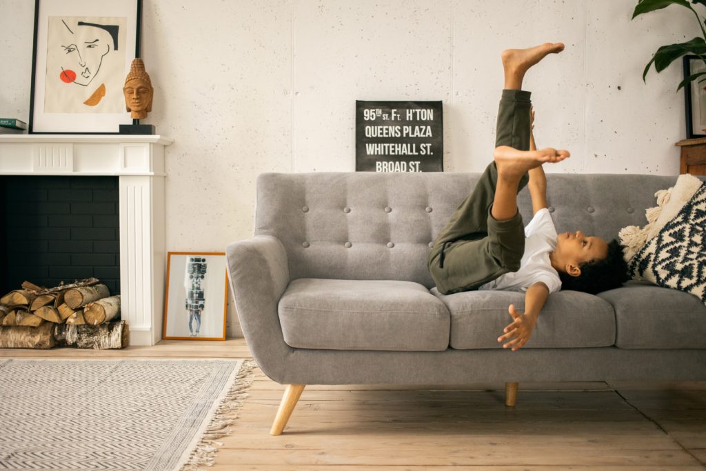 Young black boy laying on his back on couch, legs in air