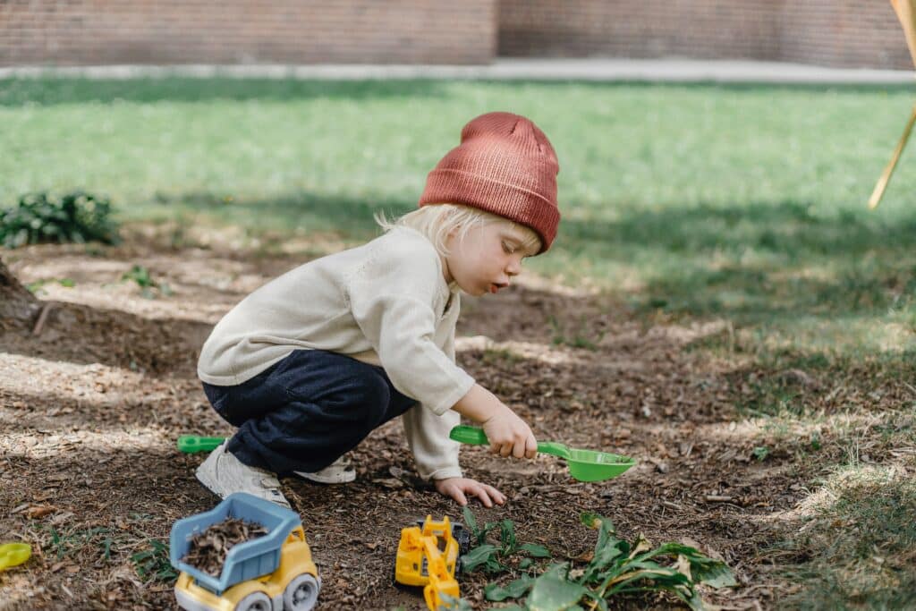 little boy playing with plastic shovel in the dirt in a backyard