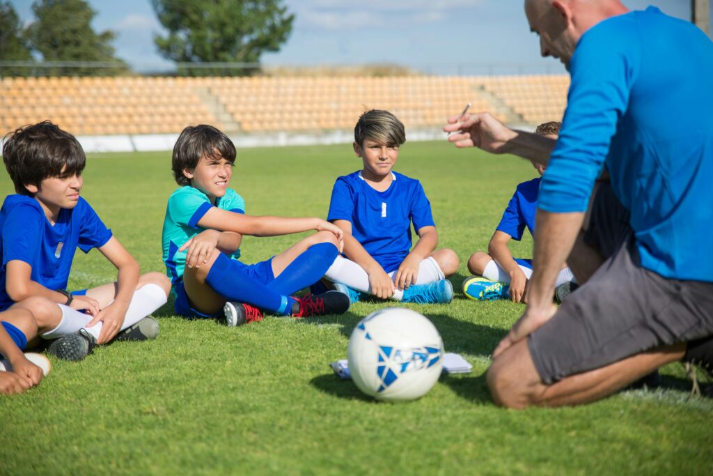 Man in blue shirt coaching group of young boys on a soccer field